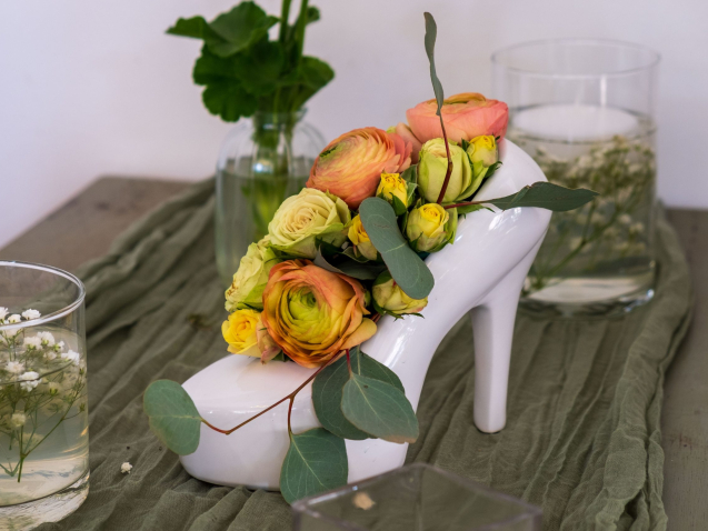 vaso bianco a forma di scarpa da donna col tacco. dentro ci sono fiori gialli