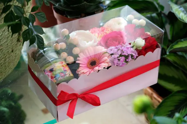 composizione in spugna di fiori freschi e candela in scatola rosa con coperchio trasparente