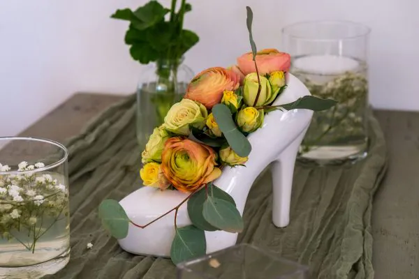 vaso bianco a forma di scarpa da donna col tacco. dentro ci sono fiori gialli